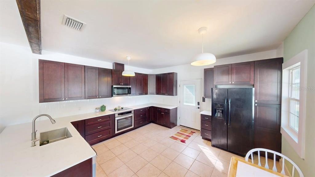 A kitchen features dark wood cabinets, white countertops, stainless steel appliances, and tile flooring — 2010 S MAPLE AVENUE, SANFORD, FL