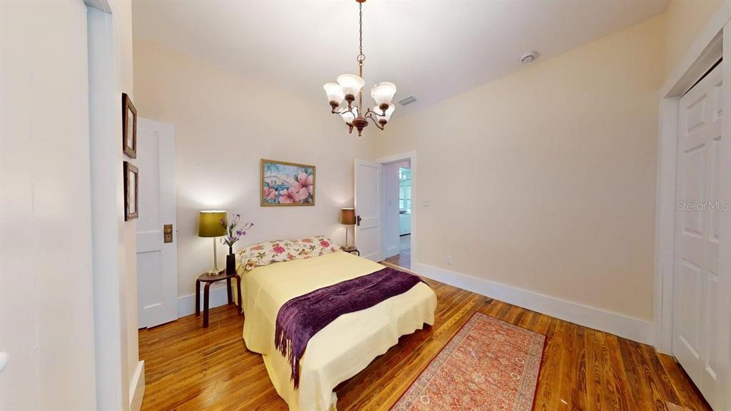 A bedroom with a yellow bed, hardwood floors, a chandelier, and a floral wall picture — 2010 S MAPLE AVENUE, SANFORD, FL