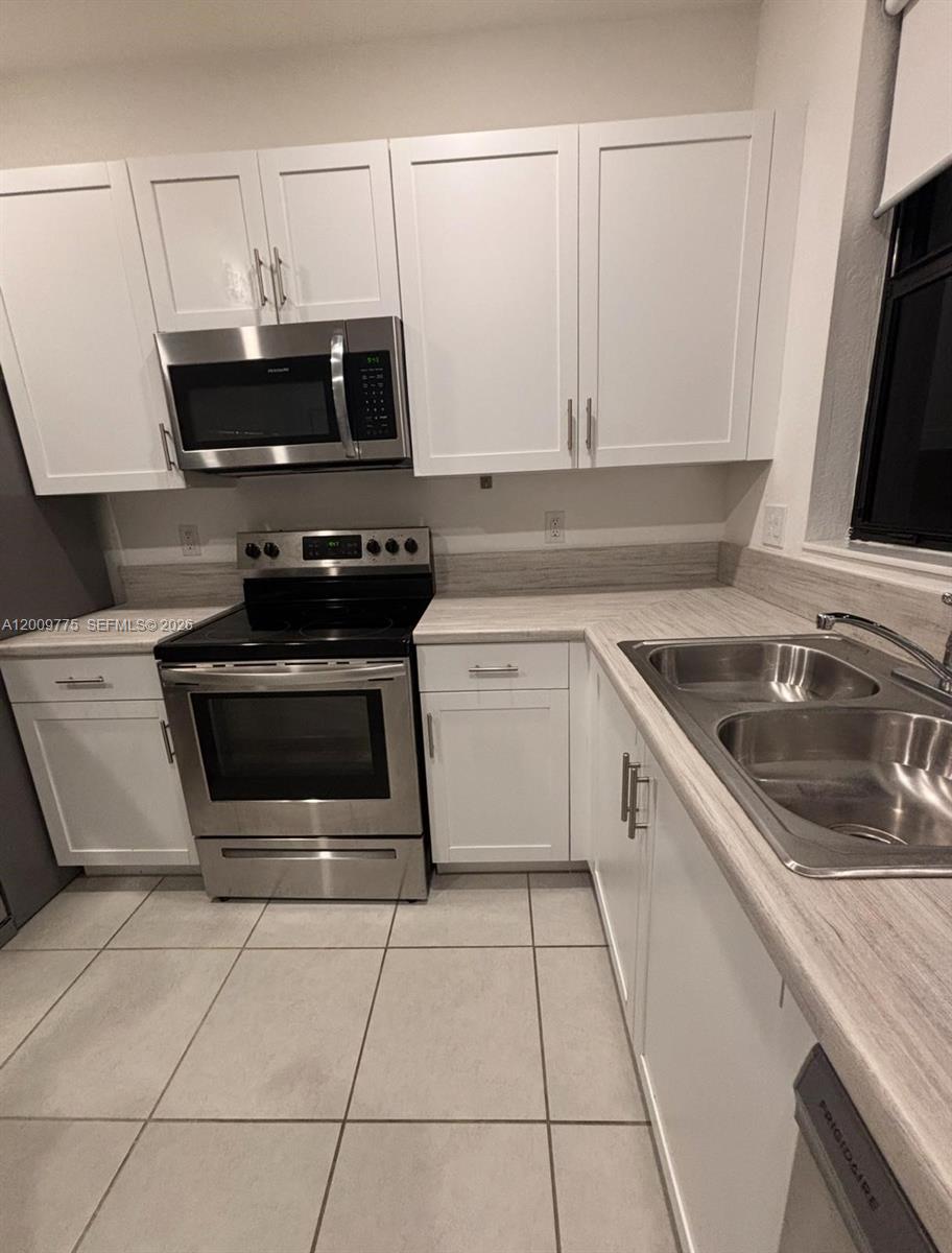 A kitchen features white cabinets, stainless steel appliances, and light-colored countertops — 20964 NE 8th Ave, Miami FL 33179, MIAMI, FL