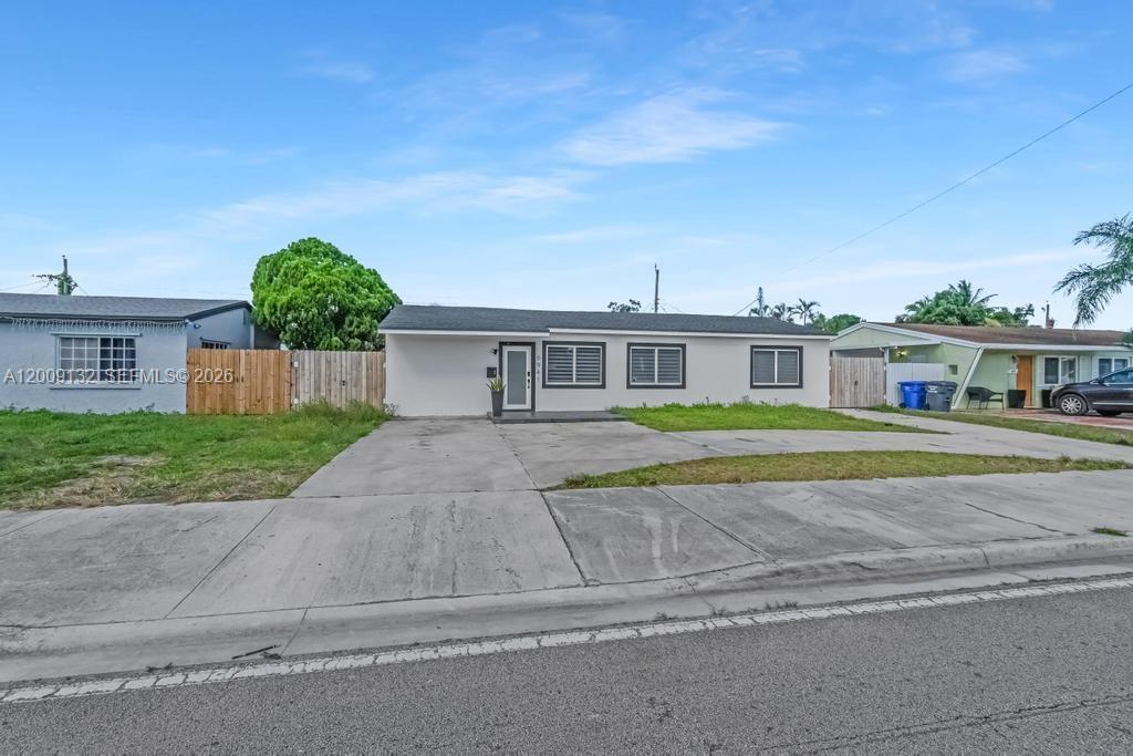 A single-story house with a concrete driveway and a fenced yard under a blue sky — 6941 Sheridan St, Hollywood FL 33024, HOLLYWOOD, FL