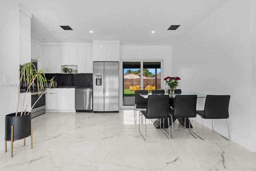 A modern kitchen and dining area with white cabinets, marble floors, and a sliding glass door — 6941 Sheridan St, Hollywood FL 33024, HOLLYWOOD, FL