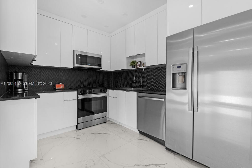 A modern kitchen features white cabinets, stainless steel appliances, and a black herringbone tile backsplash — 6941 Sheridan St, Hollywood FL 33024, HOLLYWOOD, FL