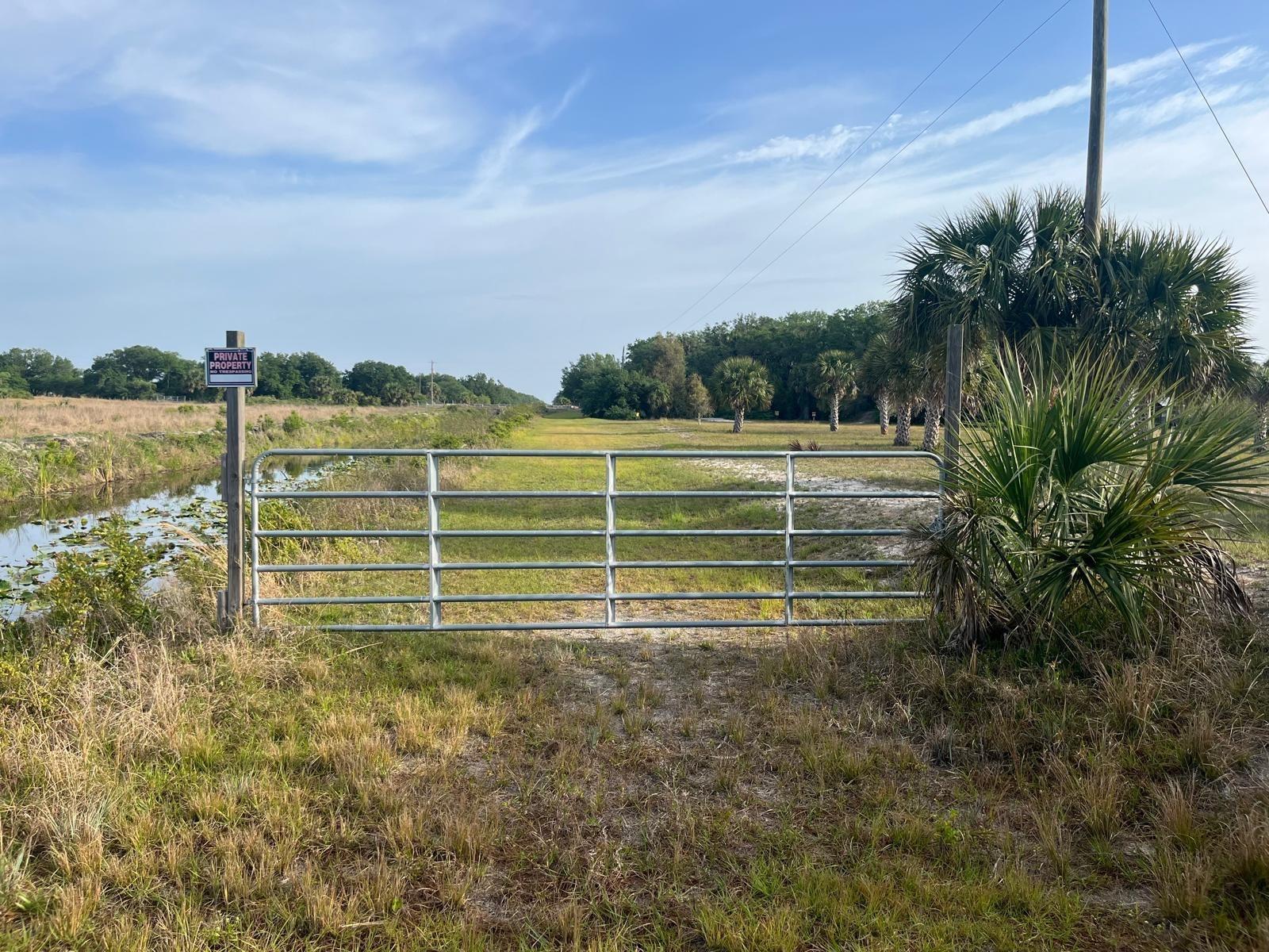 A metal farm gate stands at the entrance to a grassy field with a canal — 15148 NW 288th Street, Okeechobee FL 34972, OKEECHOBEE, FL