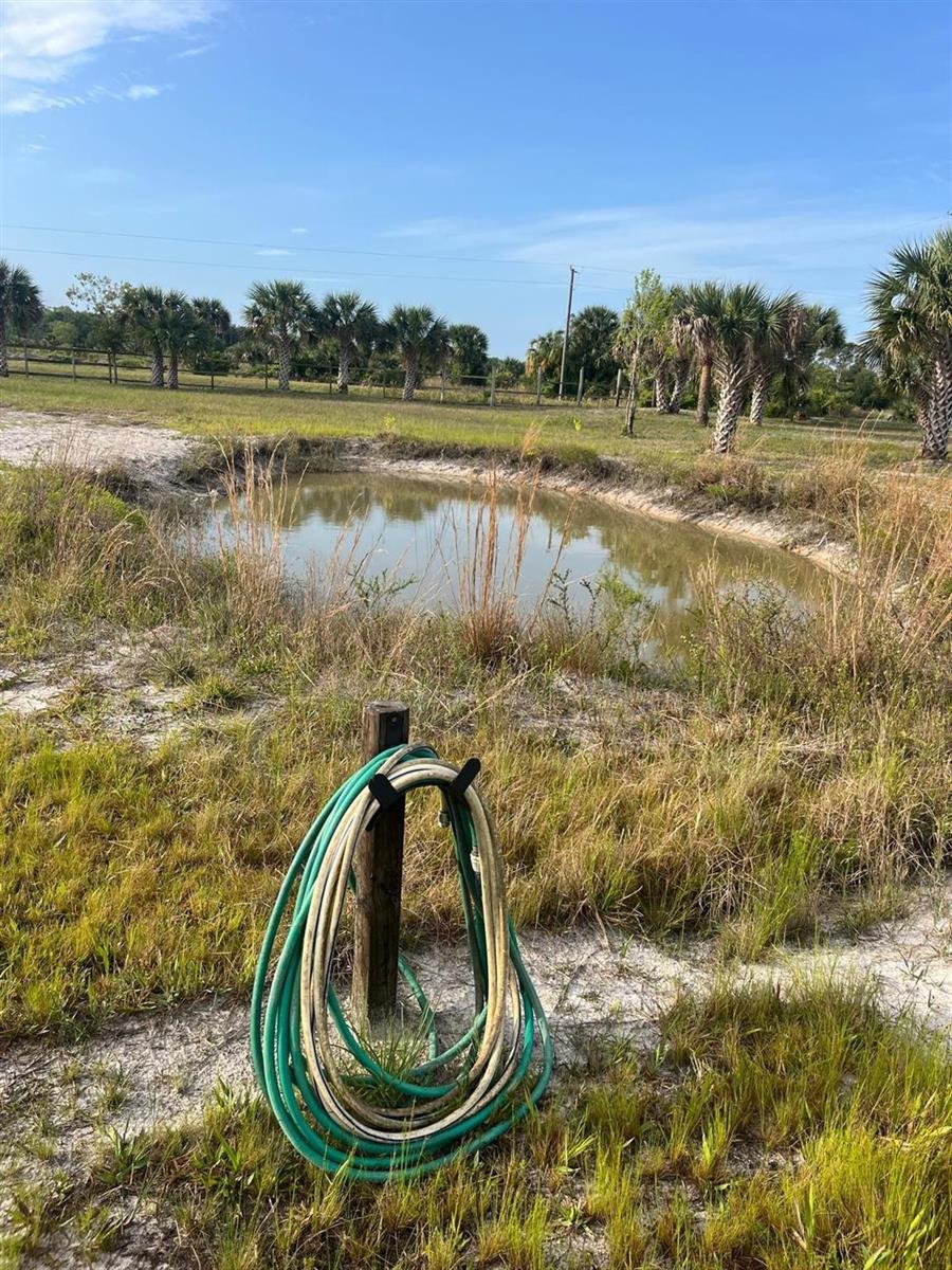 A coiled garden hose hangs on a post in front of a small, grassy pond — 15148 NW 288th Street, Okeechobee FL 34972, OKEECHOBEE, FL