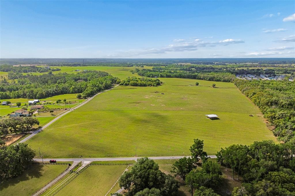An aerial view shows a large, open green pasture bordered by trees and a road — BAYHEAD ROAD Lot 9, DADE CITY, FL