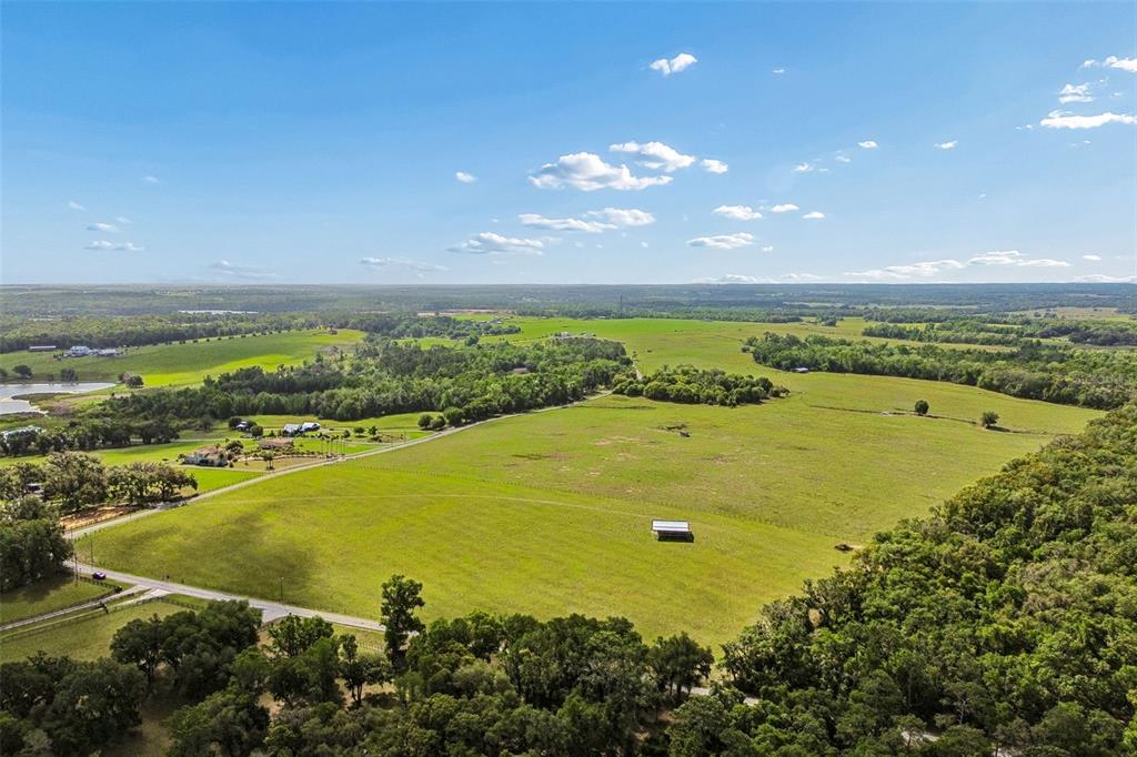 An aerial view shows a large, grassy pasture surrounded by trees and rural residential properties — BAYHEAD ROAD Lot 9, DADE CITY, FL