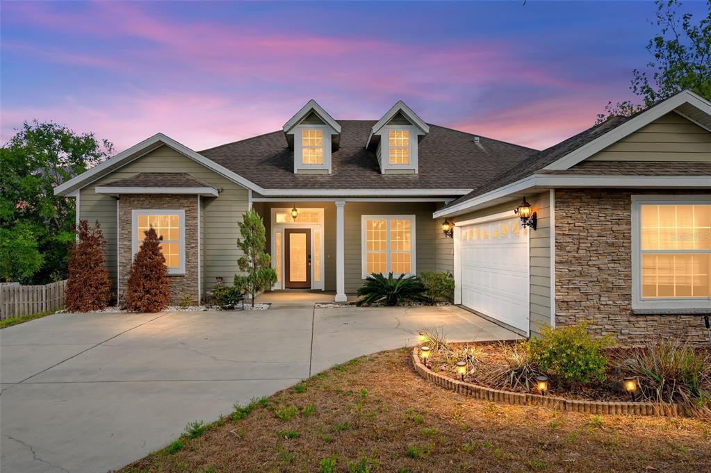 A single-story house with green siding, stone accents, a two-car garage, and two roof dormers — 14825 NW 151ST LANE, ALACHUA, FL