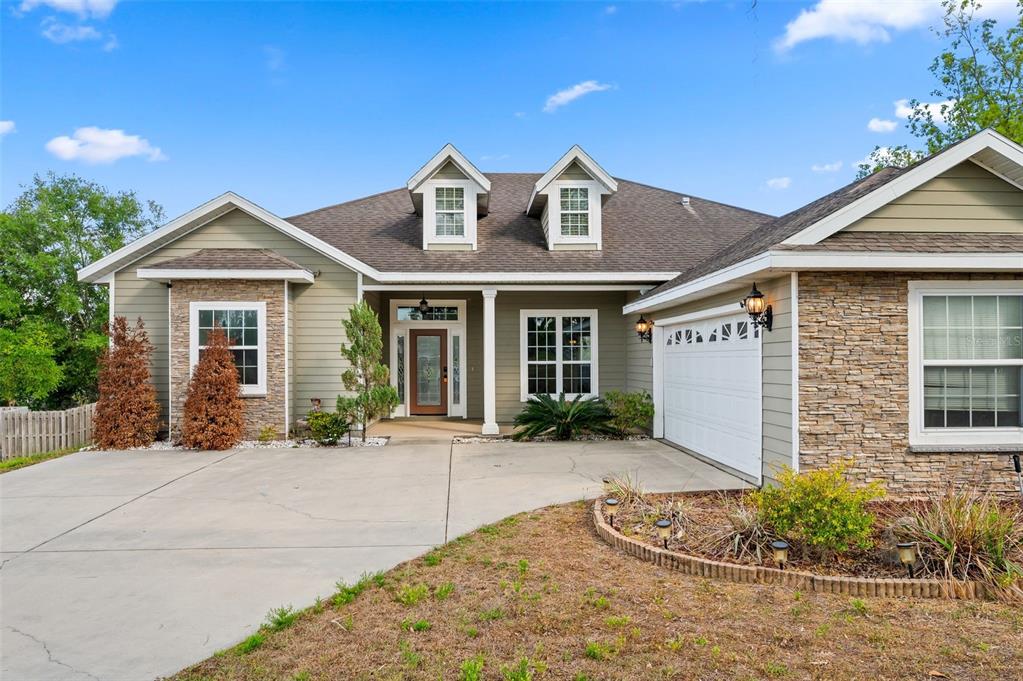 A single-story house with a stone facade, green siding, and a two-car garage — 14825 NW 151ST LANE, ALACHUA, FL