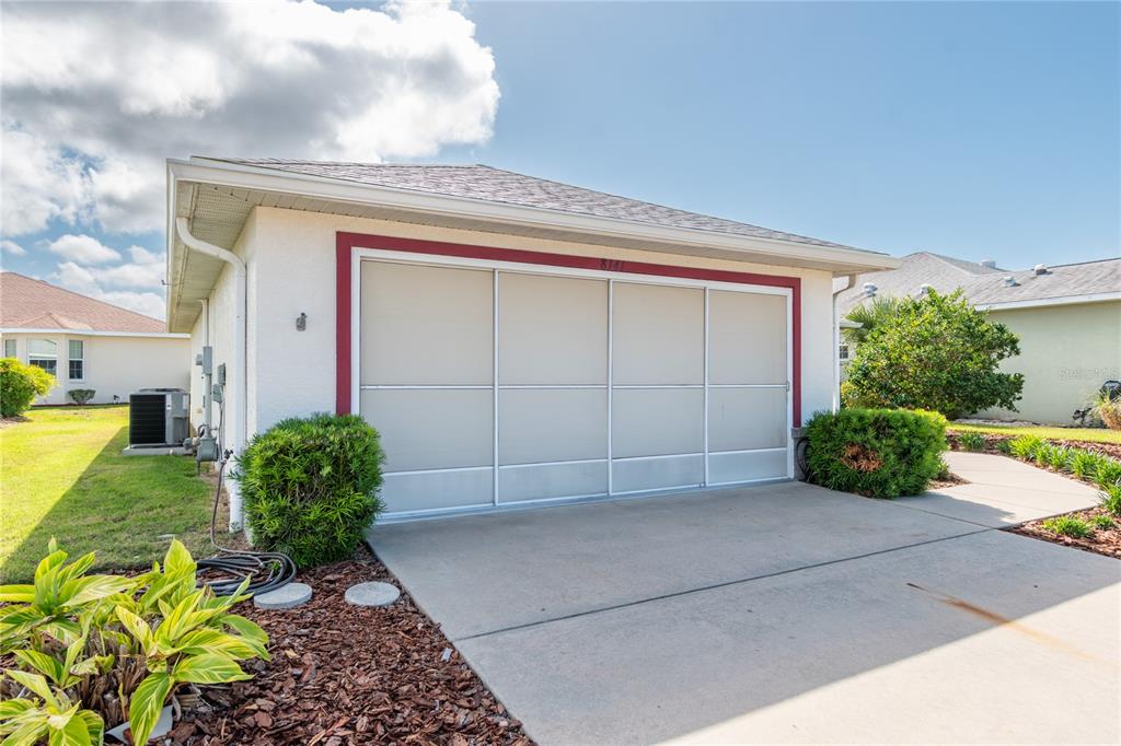 A white house exterior features a large garage door with a red frame and landscaping — 8141 SW 80TH TERRACE, OCALA, FL