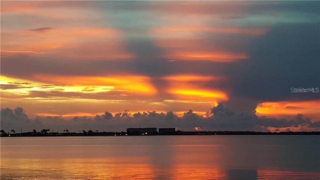 A vibrant sunset glows over a calm body of water with distant buildings on the horizon — 464 N PAULA DRIVE N UNIT 323, DUNEDIN, FL