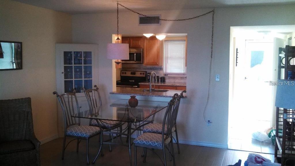 A dining area with a glass table and chairs sits in front of a kitchen pass-through — 464 N PAULA DRIVE N UNIT 323, DUNEDIN, FL
