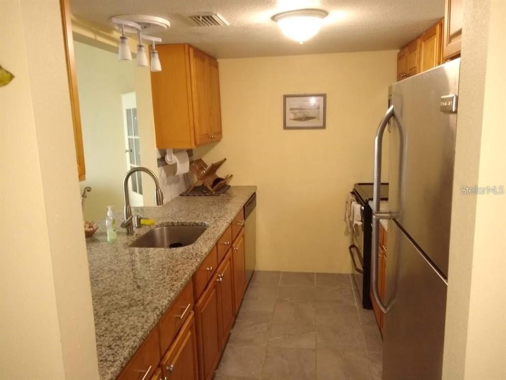 A galley kitchen features wood cabinets, granite countertops, and stainless steel appliances — 464 N PAULA DRIVE N UNIT 323, DUNEDIN, FL