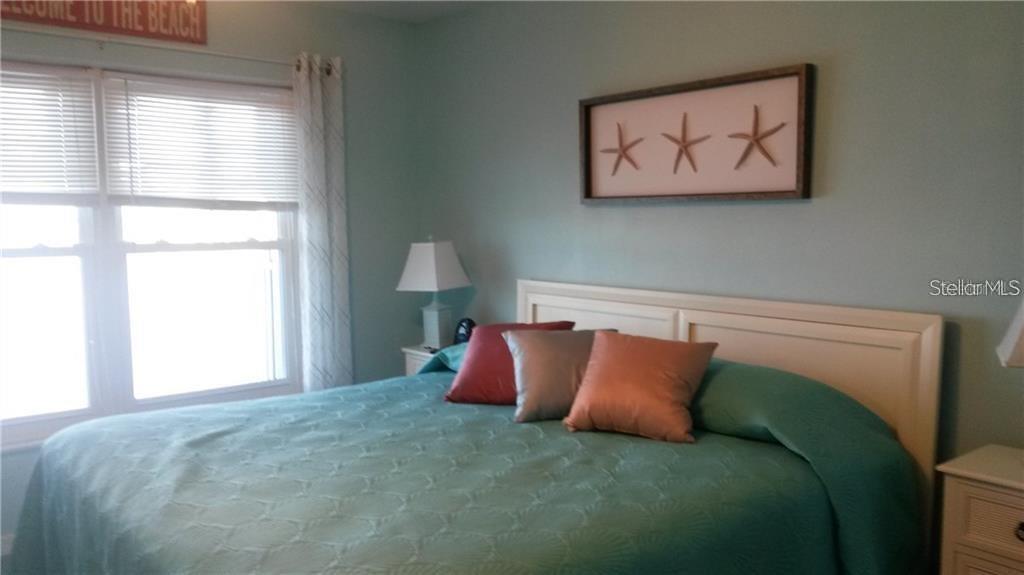 A bedroom features a bed with a teal cover, three decorative pillows, and starfish wall art — 464 N PAULA DRIVE N UNIT 323, DUNEDIN, FL