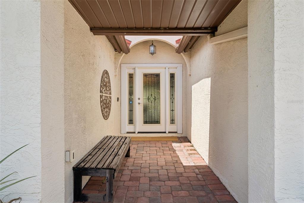 A covered entryway features a brick floor, a wooden bench, and a glass-paneled front door — 7808 THE ESPLANADE COURT, ORLANDO, FL