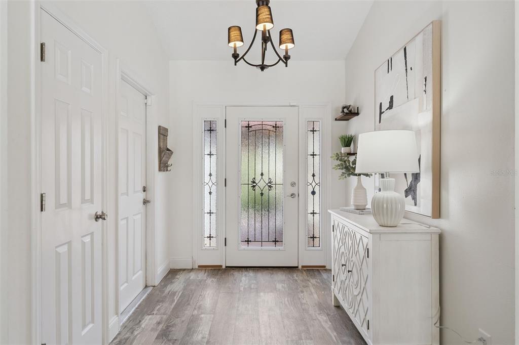 A bright entryway features a white front door with glass panels, wood-look flooring, and chandelier — 7808 THE ESPLANADE COURT, ORLANDO, FL