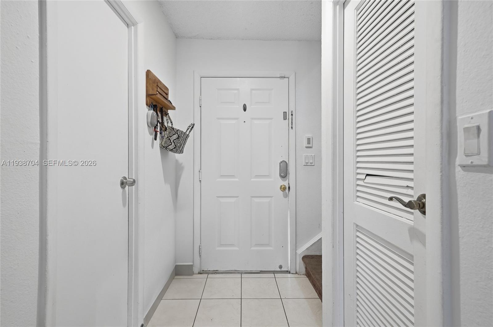 A white entryway features a front door, tiled flooring, and two adjacent closet doors — 17901 NW 68th Ave # R206, Hialeah FL 33015, HIALEAH, FL