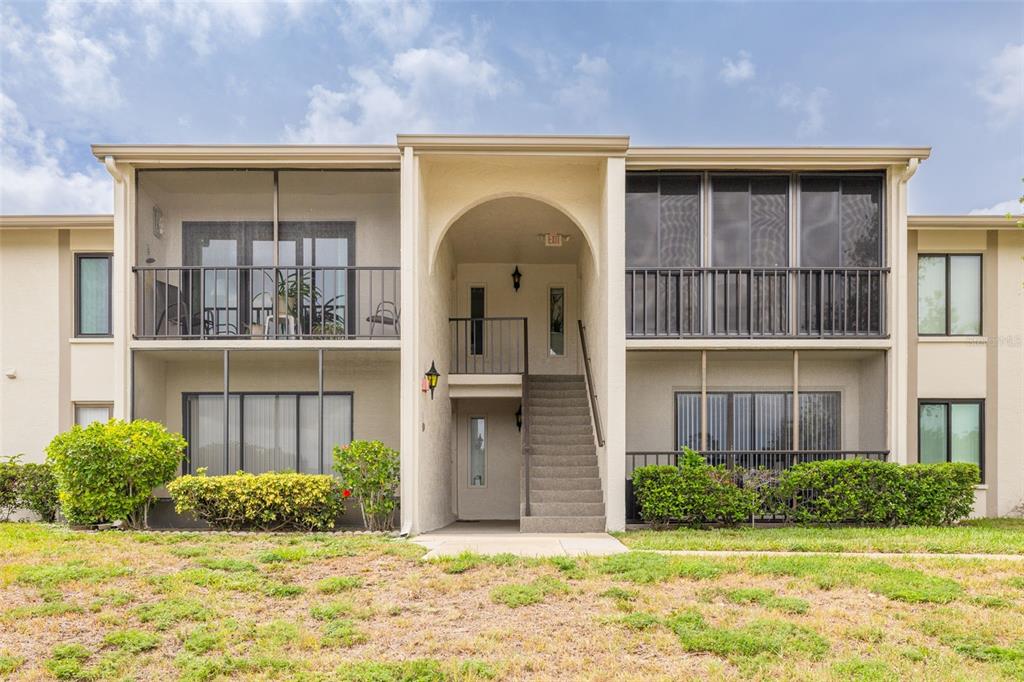 A two-story apartment building with screened balconies, a central staircase, and landscaped bushes — 1882 PINE RIDGE WAY W UNIT C2, PALM HARBOR, FL