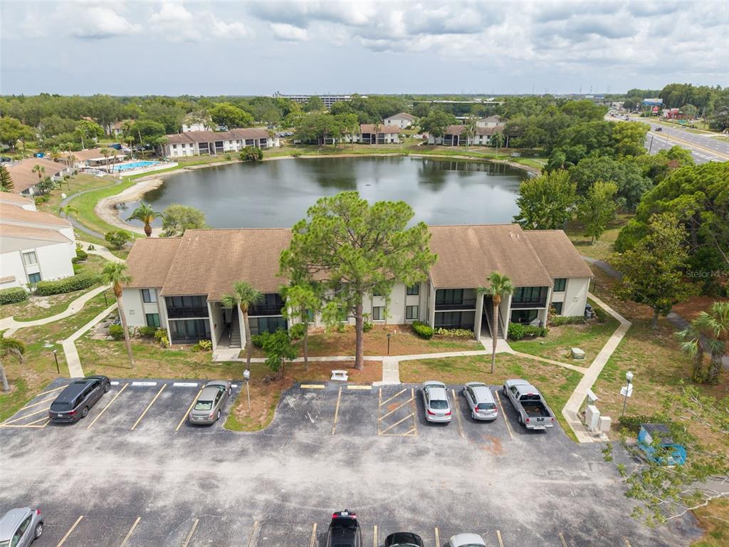 An aerial view shows a multi-story apartment building situated next to a lake and parking lot — 1882 PINE RIDGE WAY W UNIT C2, PALM HARBOR, FL