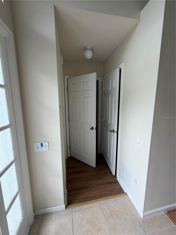 A hallway with wood flooring connects two white doors, featuring a ceiling light and tile — 3419 SANTA MONICA DRIVE, ORLANDO, FL