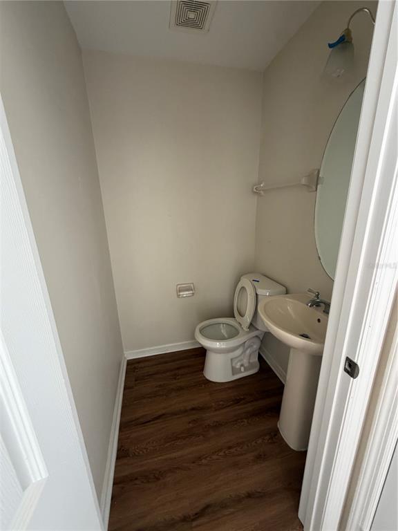 A small bathroom features a pedestal sink, a white toilet, and wood-look flooring — 3419 SANTA MONICA DRIVE, ORLANDO, FL