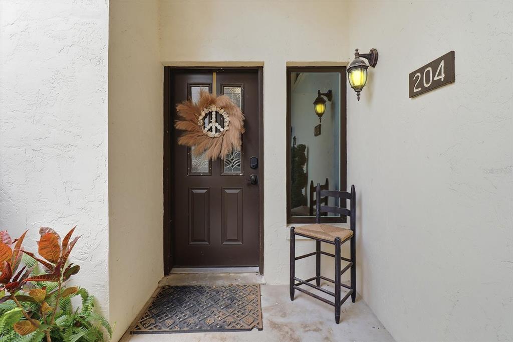 A brown front door with a peace sign wreath sits beside a window and chair — 1637 SE PARADISE CIRCLE UNIT 204, CRYSTAL RIVER, FL