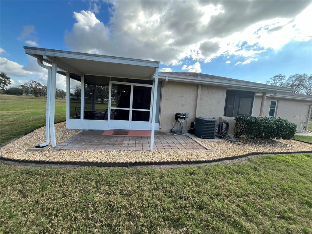 A house exterior features a screened-in patio, a paved area, and a gravel landscape bed — 1907 CANTERBURY LANE UNIT 10, SUN CITY CENTER, FL