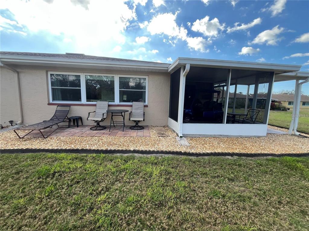 A tan house exterior features a paved patio, a screened-in porch, and a gravel yard — 1907 CANTERBURY LANE UNIT 10, SUN CITY CENTER, FL