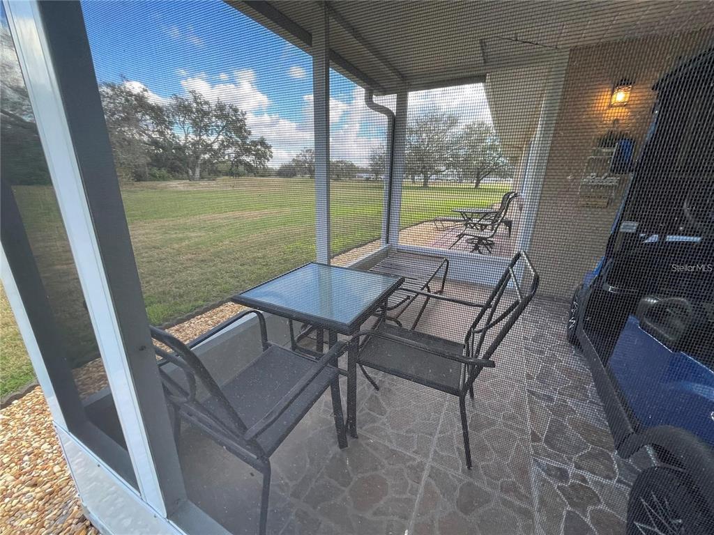 A screened-in patio features a small table, two chairs, and a view of a grassy field — 1907 CANTERBURY LANE UNIT 10, SUN CITY CENTER, FL