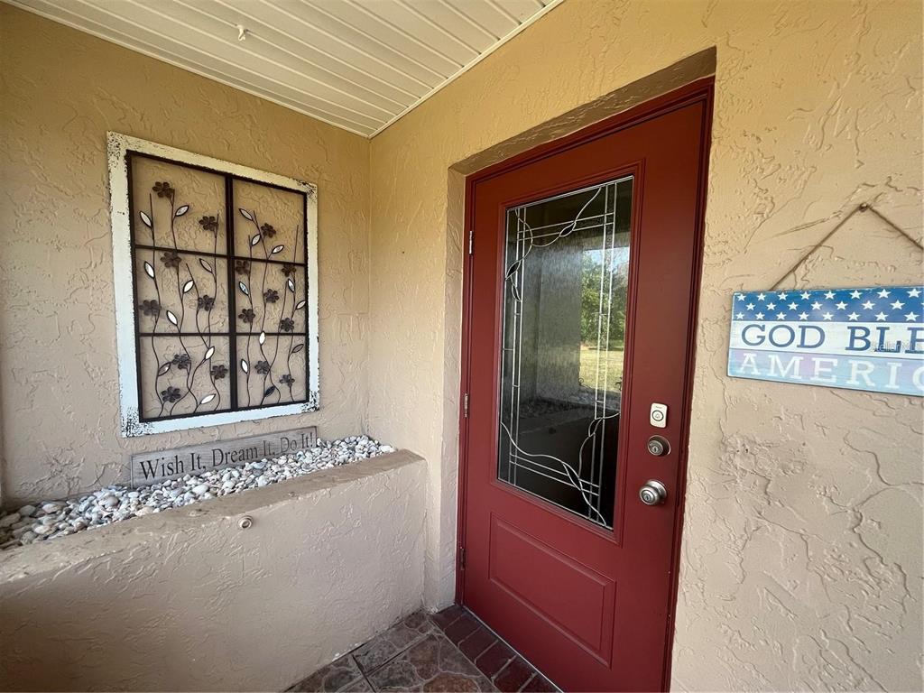A red front door with a glass insert sits beside a decorative wall hanging — 1907 CANTERBURY LANE UNIT 10, SUN CITY CENTER, FL