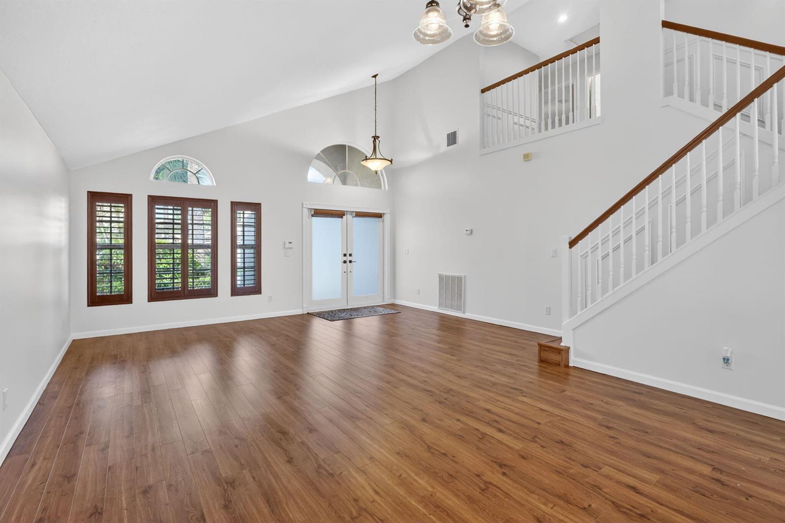 A bright, empty living room features high vaulted ceilings, wood flooring, and a staircase — 1021 SE Westminster Place, Stuart FL 34997, STUART, FL