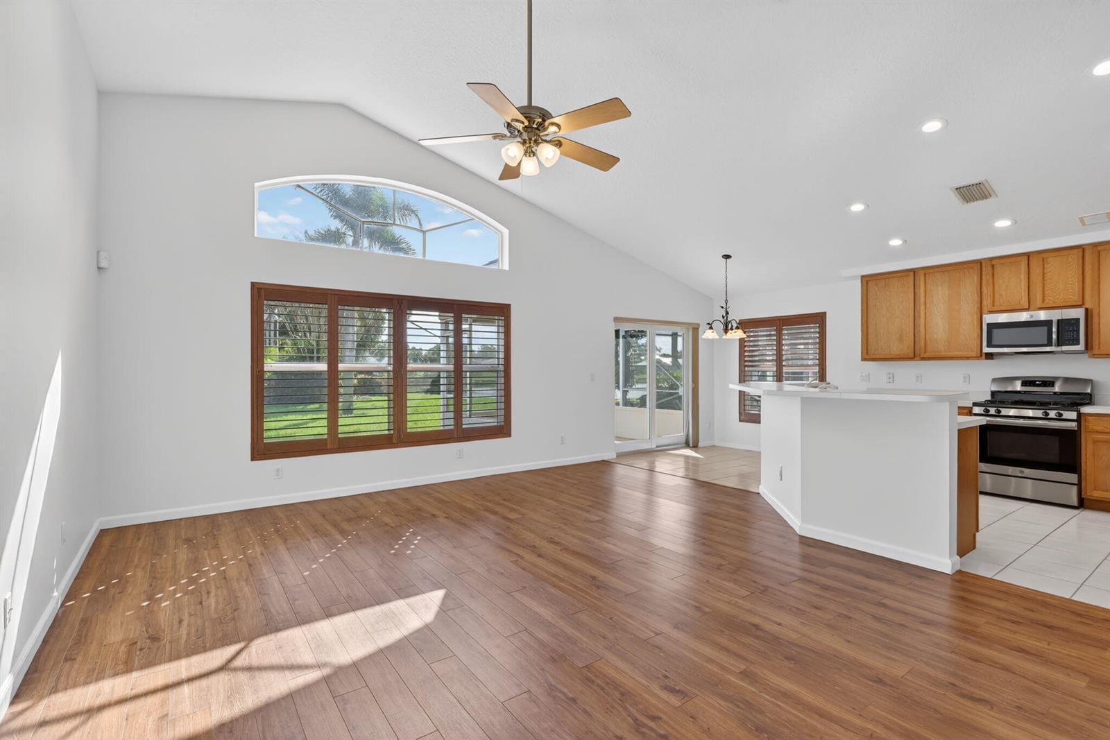 An open-concept living area features wood-look flooring, a vaulted ceiling, and an adjacent kitchen — 1021 SE Westminster Place, Stuart FL 34997, STUART, FL