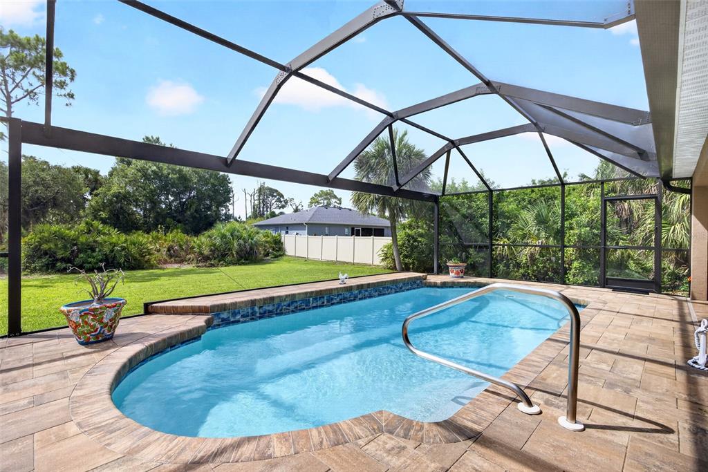 A screened-in swimming pool with a tiled border and paver deck overlooks a grassy backyard — 4841 CAMELOT STREET, NORTH PORT, FL