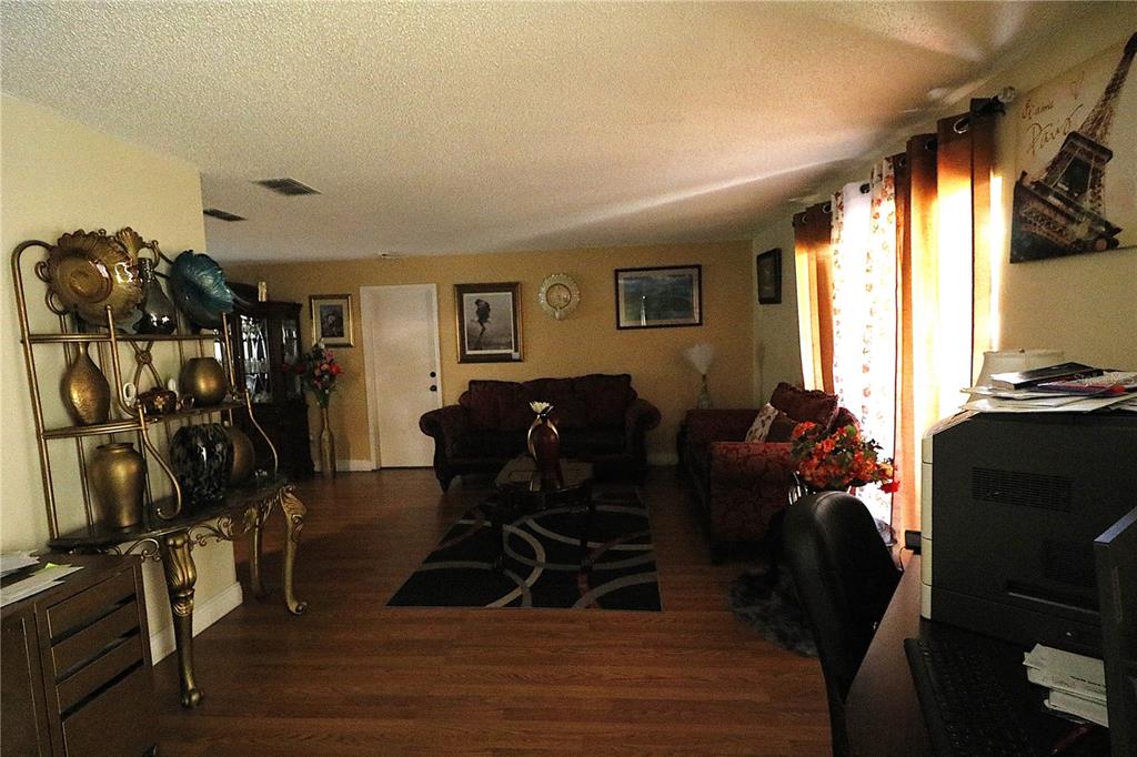 A living room features wood-look flooring, two dark sofas, and a decorative metal display shelf — 1419 CARRIAGE OAK COURT, OCOEE, FL