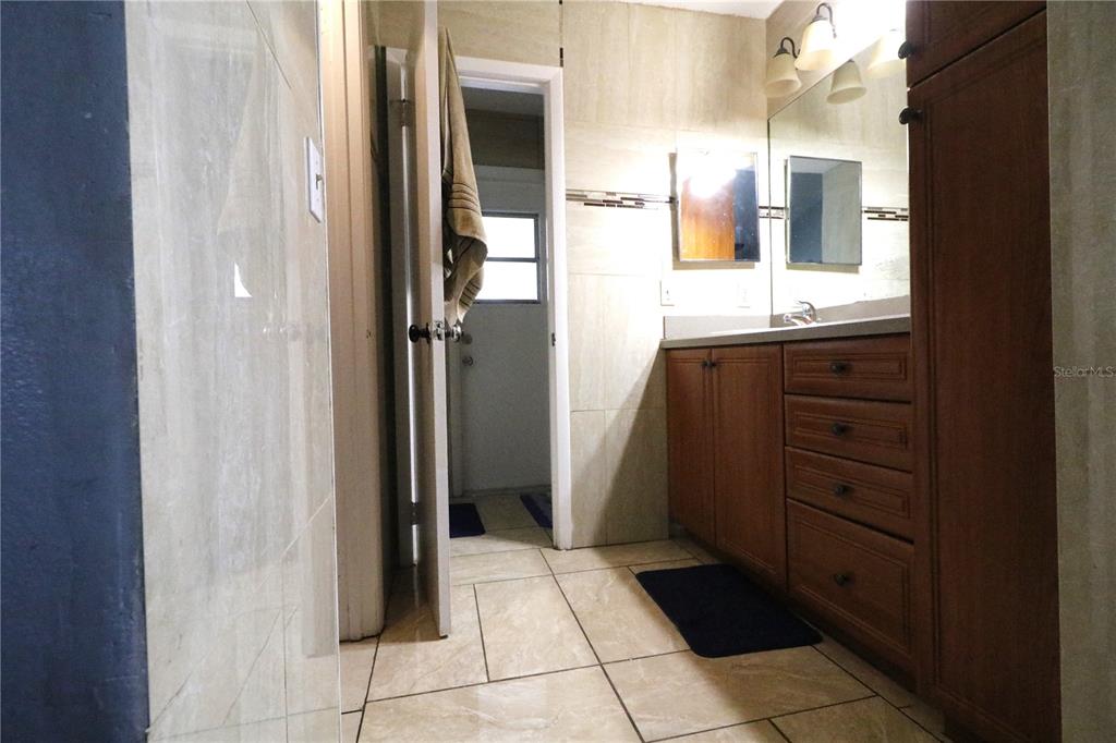 A bathroom features tiled walls and floors, a wooden vanity, and a doorway leading outside — 1419 CARRIAGE OAK COURT, OCOEE, FL