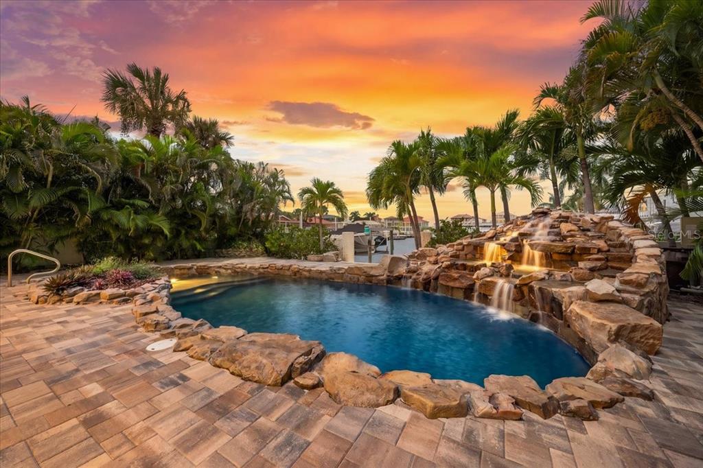 A swimming pool with a rock waterfall feature is surrounded by a paver patio and palms — 5151 PORPOISE PLACE, NEW PORT RICHEY, FL