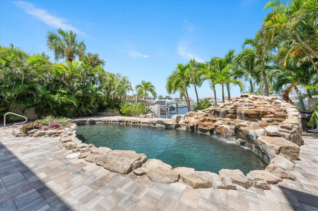 A backyard swimming pool features a natural rock waterfall, stone coping, and surrounding palm trees — 5151 PORPOISE PLACE, NEW PORT RICHEY, FL