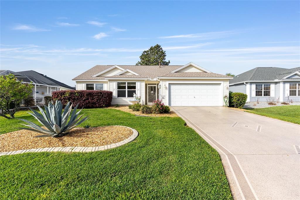 A single-story house with a white garage, beige siding, and a landscaped front yard — 8288 SE 176TH LAWSON LOOP, THE VILLAGES, FL
