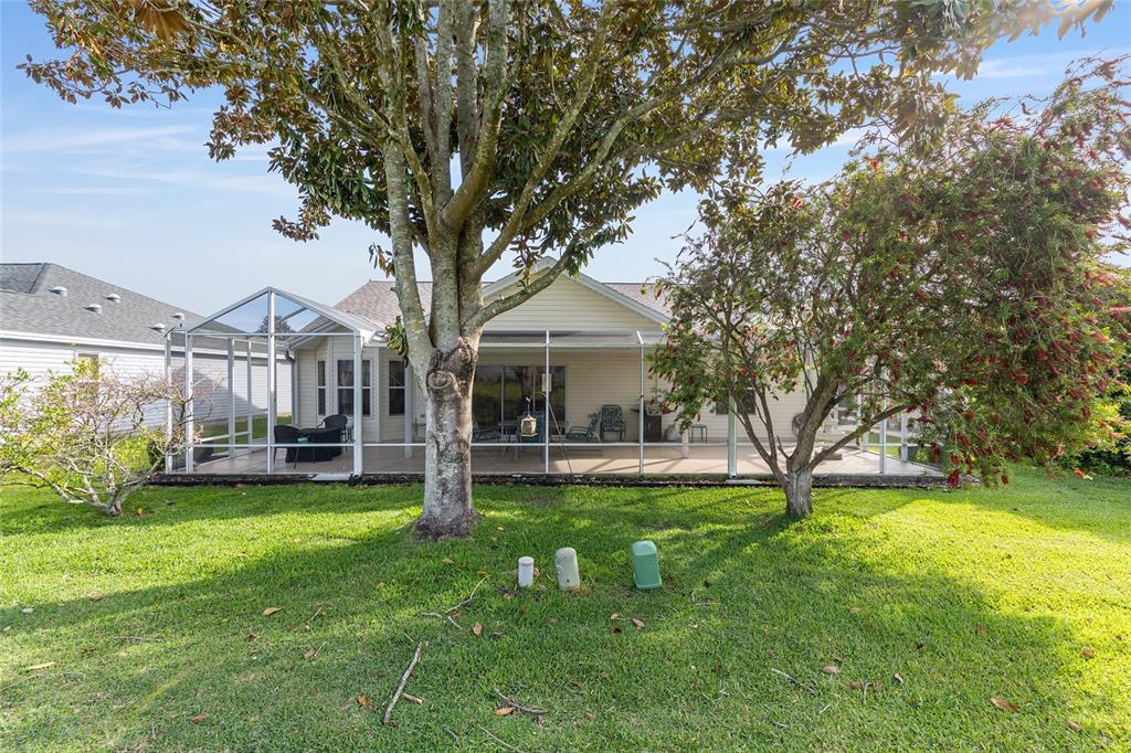 The backyard features a screened-in patio attached to a single-story house with mature trees — 8288 SE 176TH LAWSON LOOP, THE VILLAGES, FL