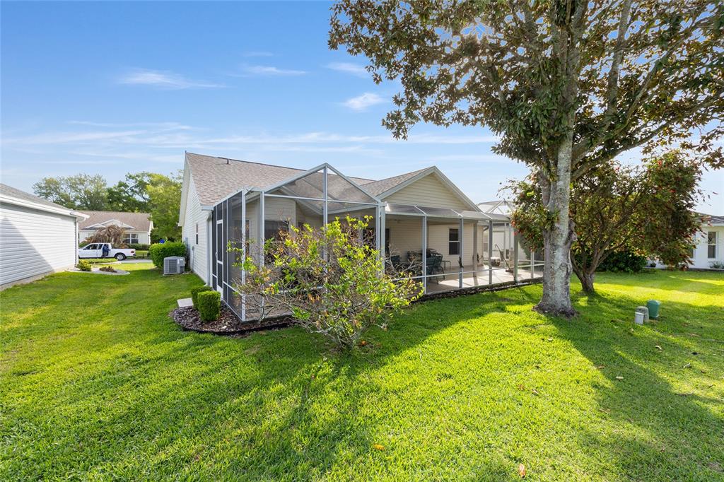 A backyard view of a house with a screened-in patio and a large tree — 8288 SE 176TH LAWSON LOOP, THE VILLAGES, FL