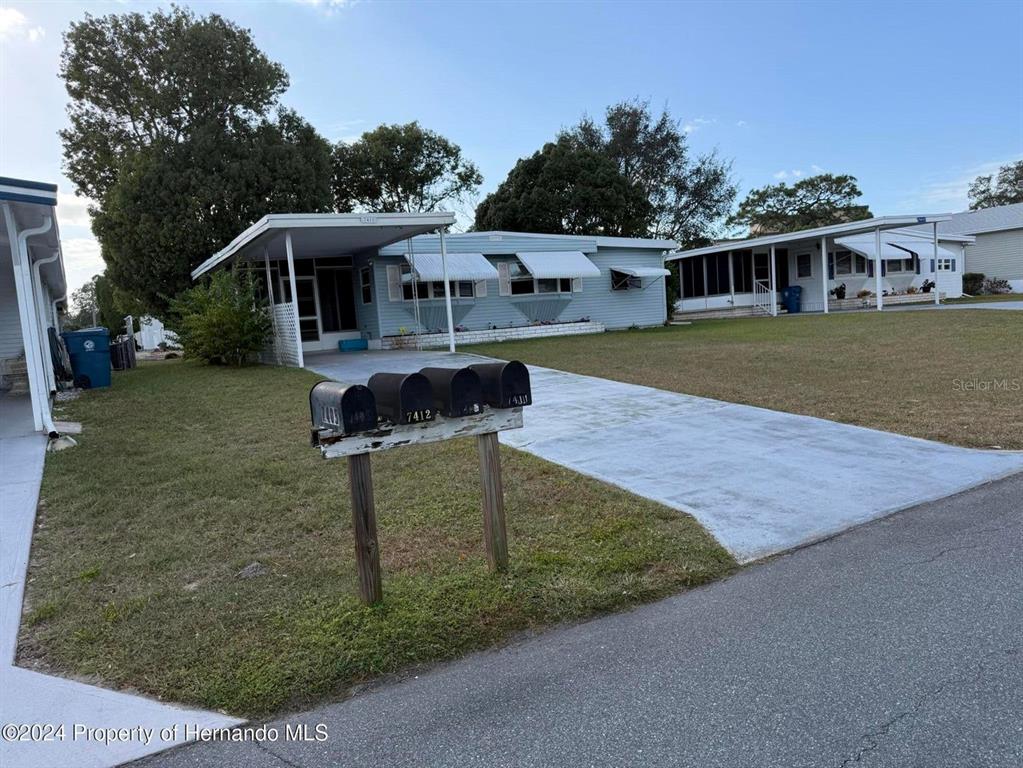A light blue manufactured home features a carport, metal awnings, and a row of mailboxes — 7411 FAIRLANE AVENUE, BROOKSVILLE, FL