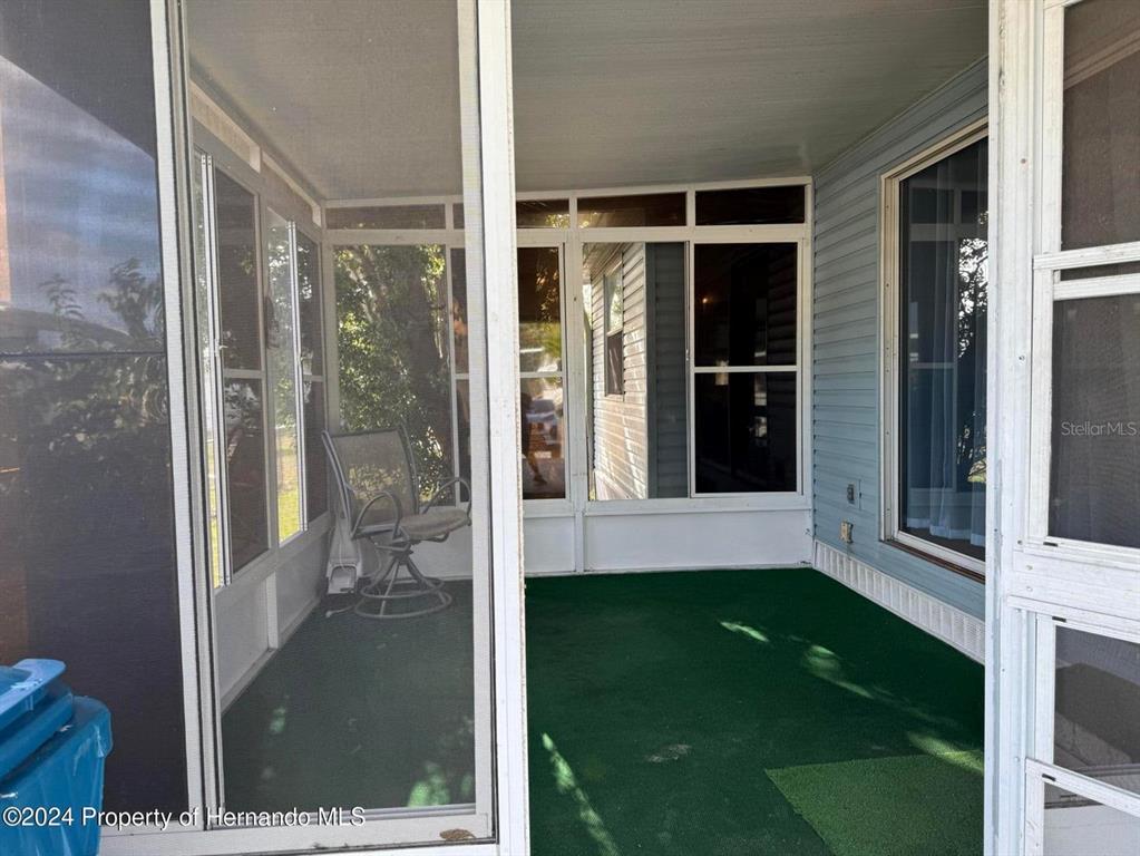 A screened-in porch features green outdoor carpeting, white framing, and a single swivel chair — 7411 FAIRLANE AVENUE, BROOKSVILLE, FL