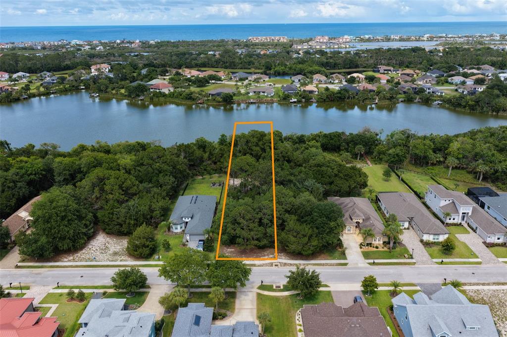An aerial view shows a vacant, wooded residential lot outlined in orange bordering a lake — 18 N LAKEWALK DRIVE, PALM COAST, FL