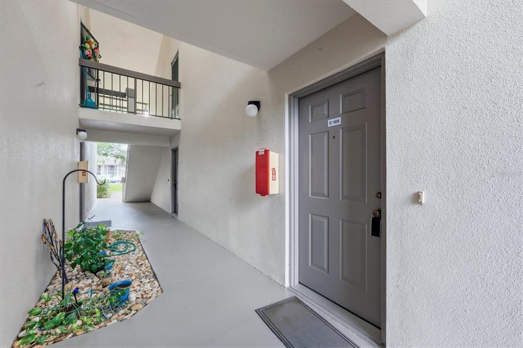 An exterior view of a ground-floor apartment entrance with a gray door and landscaping — 1515 FORREST NELSON BOULEVARD UNIT C105, PORT CHARLOTTE, FL