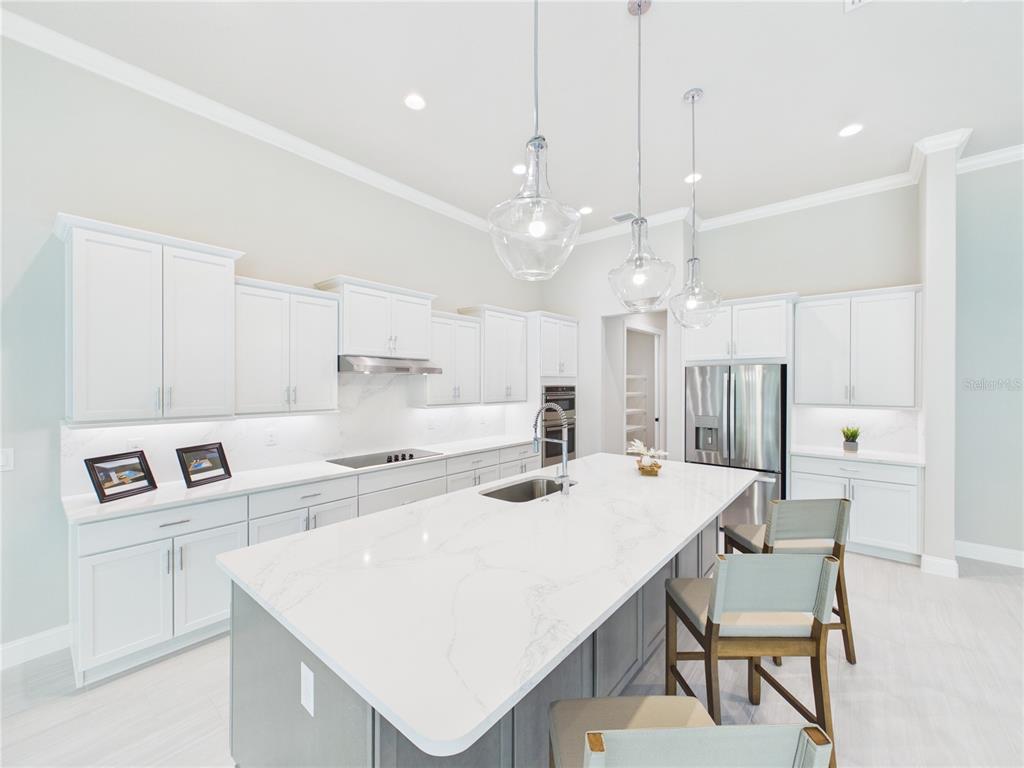 A modern kitchen features white cabinetry, a large marble-topped island, and three glass pendant lights — 230 S RIVERWALK DRIVE, PALM COAST, FL