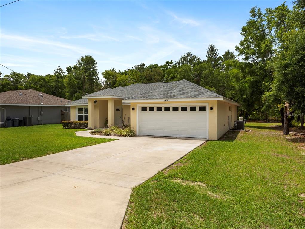 A single-story house with a yellow exterior, a two-car garage, and a concrete driveway — 9432 SE 159TH LANE, SUMMERFIELD, FL