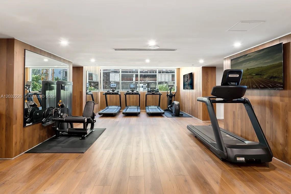A modern gym features wood-paneled walls, hardwood flooring, multiple treadmills, and a strength training machine — 555 NE 34th St # 2409, Miami FL 33137, MIAMI, FL