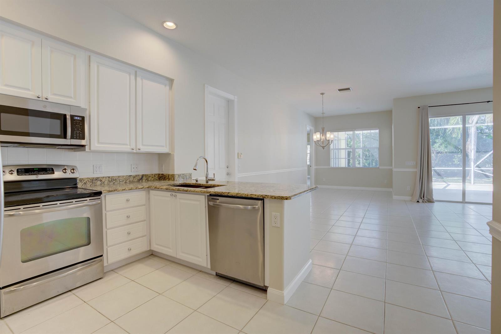 A kitchen with white cabinets, granite countertops, and stainless steel appliances opens to a dining area — 256 San Remo Drive, Jupiter FL 33458, JUPITER, FL