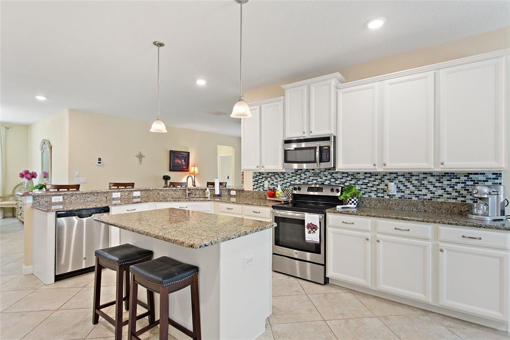 A kitchen features white cabinets, granite countertops, a tiled backsplash, and a central island — 1311 GLENEAGLES LANE, DAVENPORT, FL