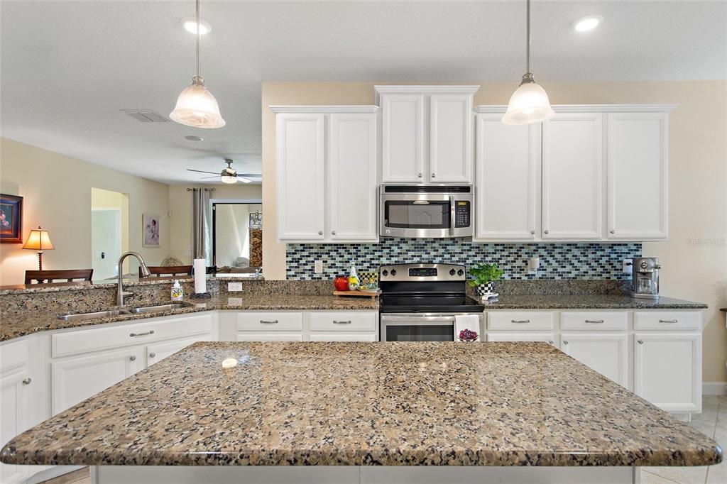 A kitchen features white cabinets, granite countertops, a tiled backsplash, and a central island — 1311 GLENEAGLES LANE, DAVENPORT, FL