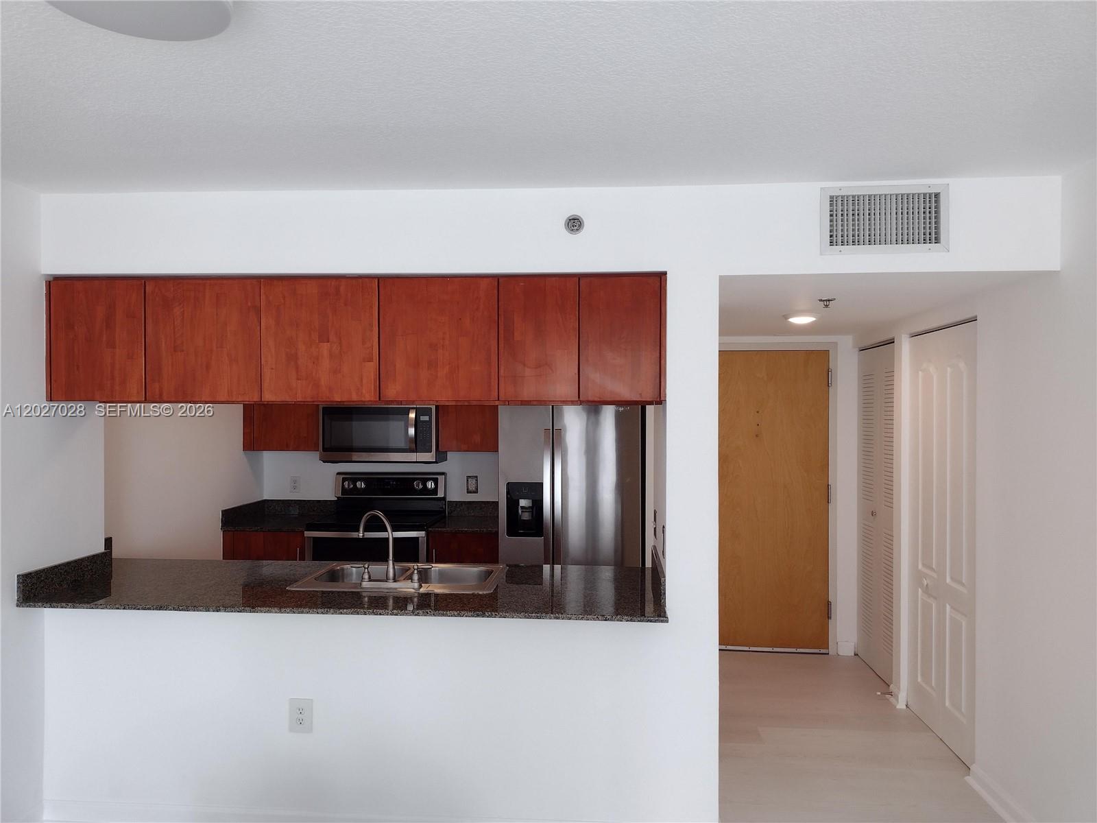 A kitchen with wood cabinets, stainless steel appliances, and a granite countertop breakfast bar — 1200 Brickell Bay Dr # 2005, Miami FL 33131, MIAMI, FL